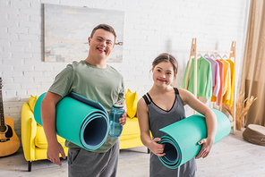 Cheerful teenagers with down syndrome holding fitness mats and sports bottle at home