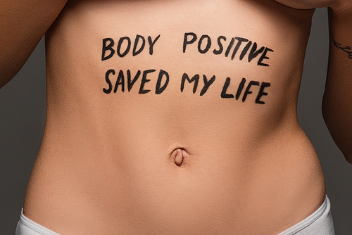 cropped view of young woman with body positive saved my life lettering on belly isolated on grey
