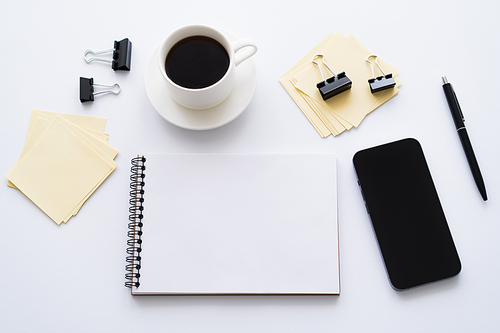top view of smartphone with blank screen near cup of coffee and stationery on white