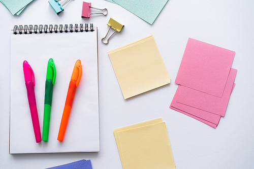 top view of colorful pens on notebook near blank paper notes and fold back clips on white