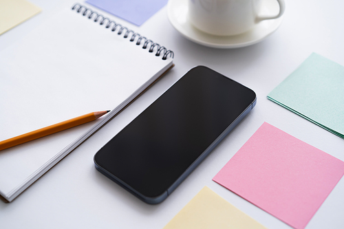 close up of stationery near smartphone with blank screen on white