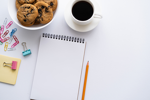 top view of cup of coffee, cookies and stationery near smartphone with blank screen on white
