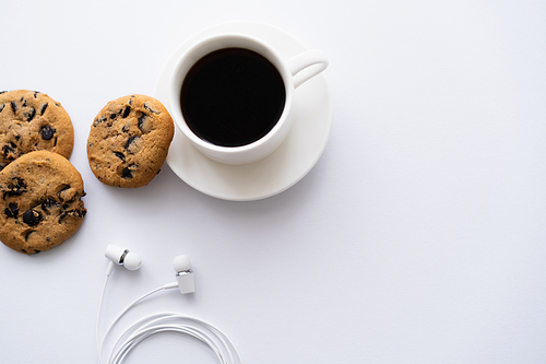 top view of cup of coffee near chocolate chip cookies and wired earphones on white