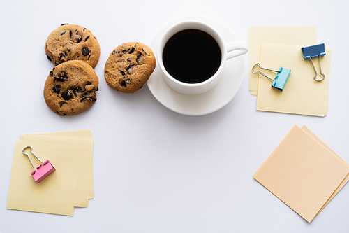 top view of cup of coffee and chocolate chip cookies near stationery on white