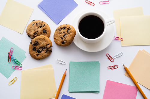 top view of chocolate chip cookies and cup of coffee near stationery on white