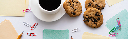 top view of chocolate chip cookies and cup of coffee near stationery on white, banner