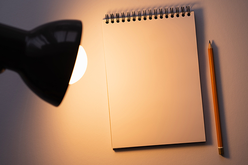 top view of blank notebook near pencil and turned on lamp on white