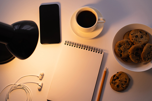 top view of lamp near smartphone,  cup of coffee and notebook on white