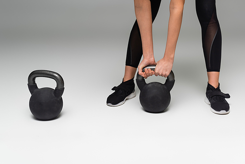 cropped view of sportswoman lifting kettlebell on grey background