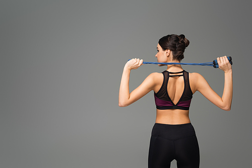 back view of young sportswoman holding jump rope isolated on grey