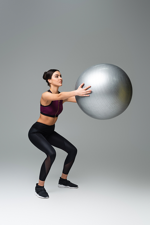 sportswoman doing sit ups with fitness ball on grey background