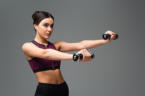 confident sportswoman working out with dumbbells isolated on grey