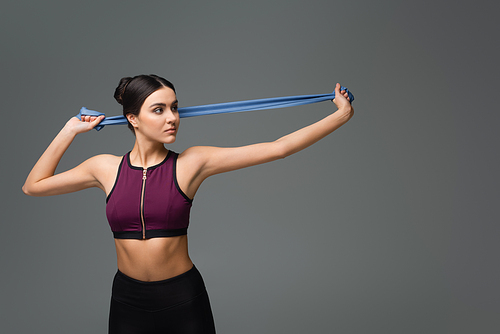 young sportswoman training with resistance band isolated on grey