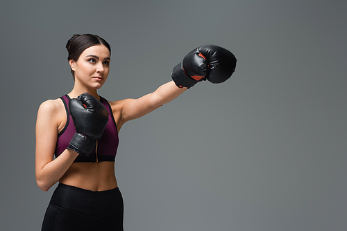 confident sportswoman training in boxing gloves isolated on grey