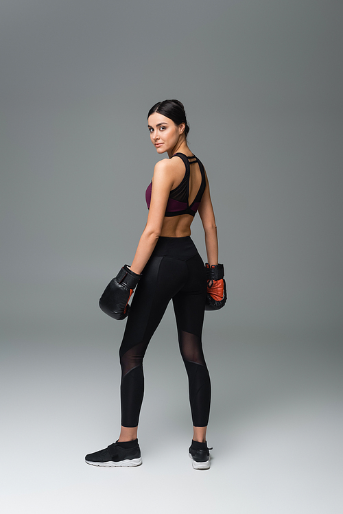 full length view of woman in black sportswear and boxing gloves on grey background