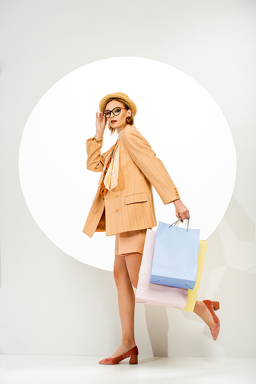 Attractive stylish girl holding shopping bags and walking near circle on white background