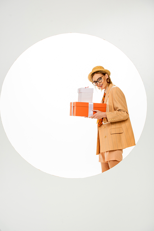 Stylish girl smiling at camera and holding gift boxes behind circle on white background