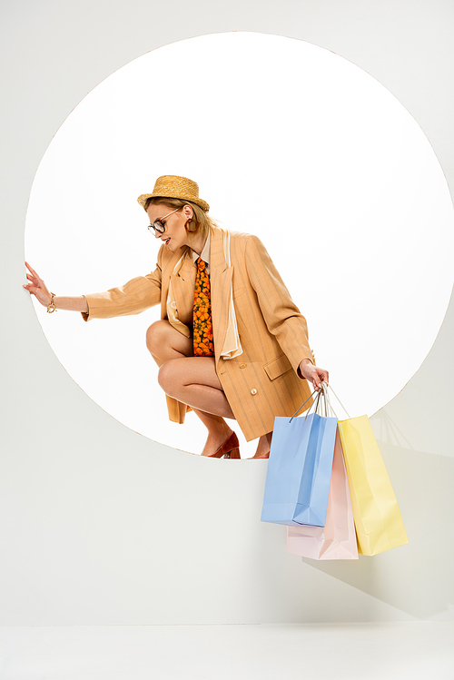 Beautiful woman in straw hat and beige jacket holding shopping bags in round hole on white background