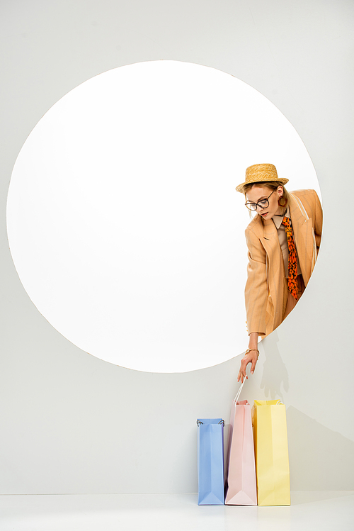 Fashionable girl holding colorful shopping bag behind circle on white background
