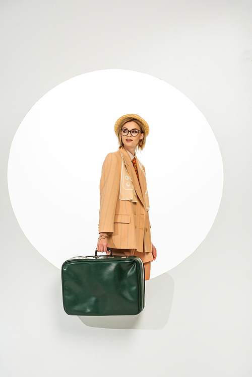 Beautiful stylish girl holding green travel bag near circle on white background