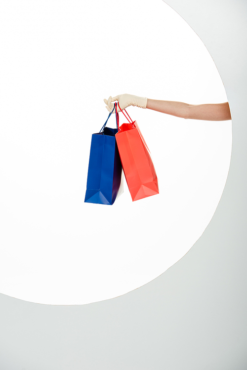 Cropped view of woman in glove holding blue and red shopping bags on white background