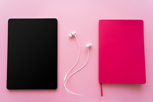 top view of digital tablet with blank screen near earphones and bright notebook on pink