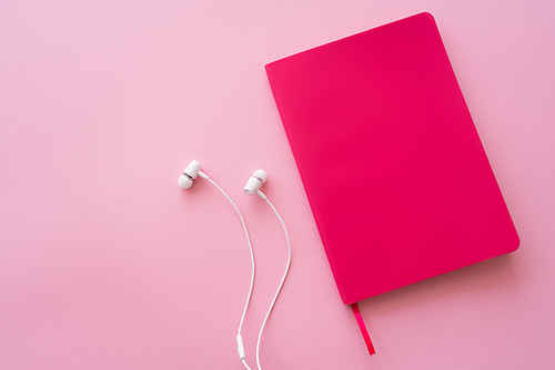 top view of earphones near bright notebook on pink
