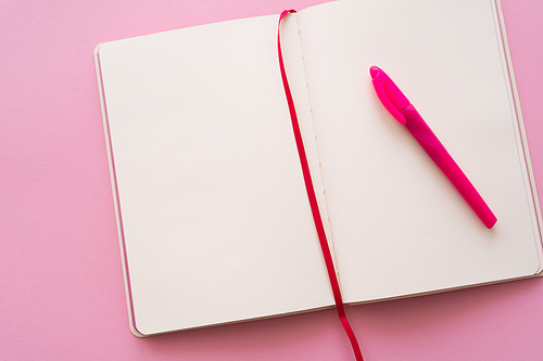 top view of empty open notebook and pen on pink