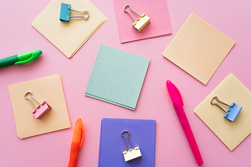 flat lay of fold back clips on colorful paper notes near pens on pink