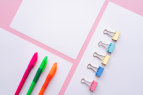 flat lay of colorful fold back clips and pens on white papers on pink