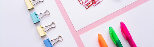 flat lay of colorful fold back clips, paper clips and pens on white papers on pink, banner