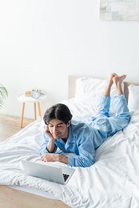 smiling man on blue pajamas watching movie on laptop on bed
