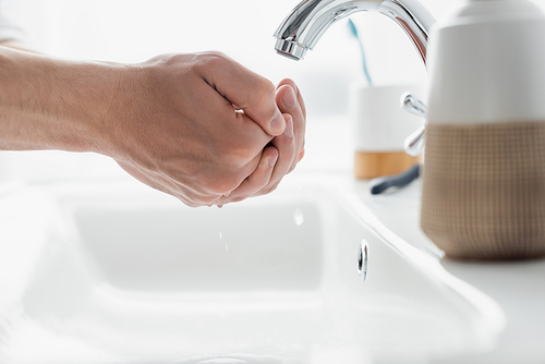 close up view of male hands near faucet and blurred toiletries