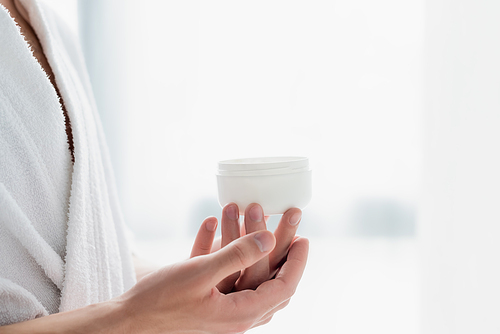 cropped view of man in bathrobe holding container with cosmetic cream