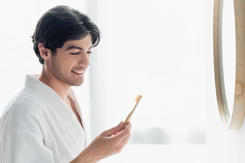 happy man in white bathrobe looking at toothbrush in bathroom