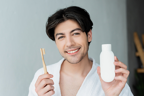 happy brunette man holding toothbrush and toothpaste while 
