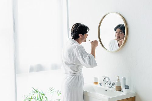 smiling man brushing teeth near mirror and sink in bathroom