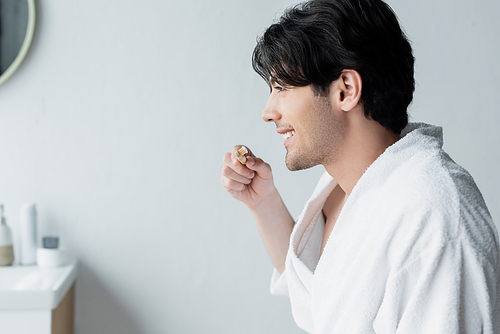 side view of smiling man holding toothbrush with toothpaste in bathroom