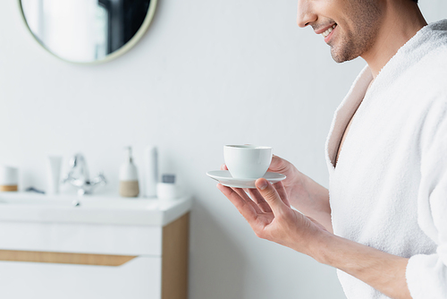 partial view of smiling man holding coffee cup in blurred bathroom