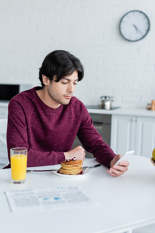 brunette man using mobile phone near pancakes and orange juice in kitchen