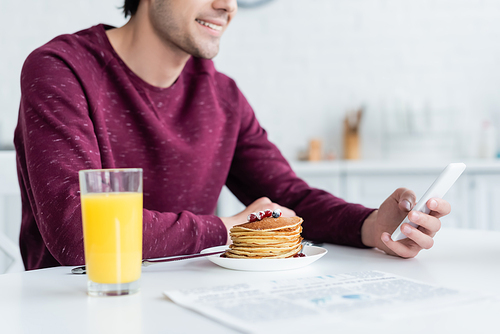 cropped view of smiling man using smartphone near pancakes and orange juice