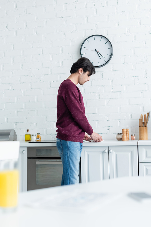 young man standing in kitchen near cup of coffee, blurred foreground