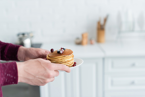 partial view of man holding delicious pancakes with cranberries in blurred kitchen