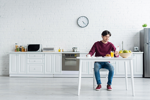 full length view of man looking at smartphone while having breakfast in spacious kitchen