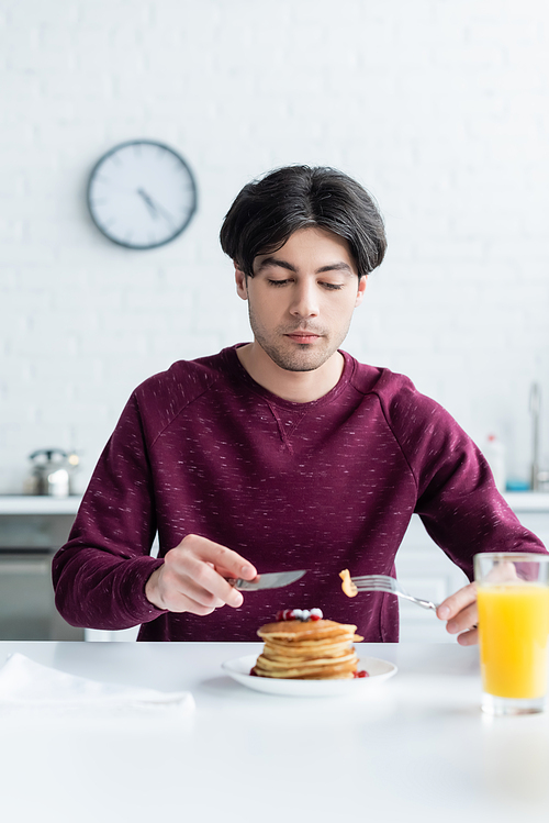 brunette man eating tasty pancakes near blurred glass of orange juice