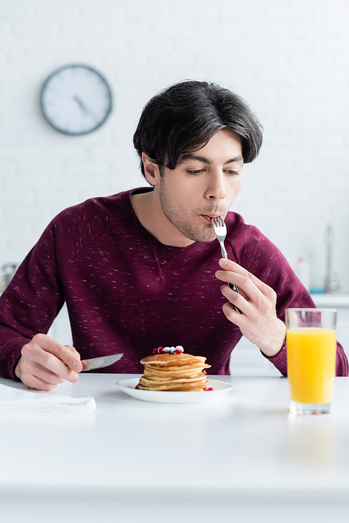 young brunette man eating tasty pancakes near glass of fresh orange juice