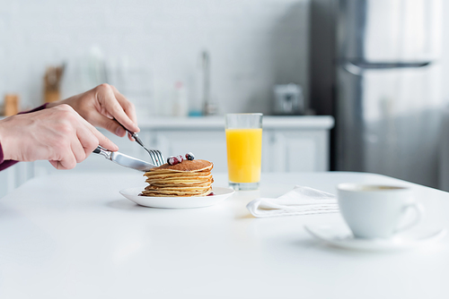 partial view of mam cutting pancakes near orange juice and blurred coffee cup