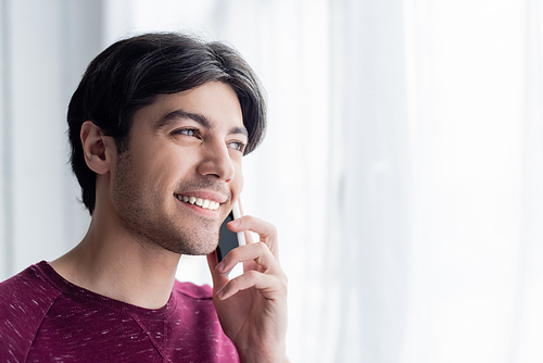 young brunette man smiling during phone conversation at home
