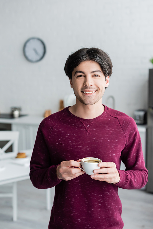 happy young man holding cup of coffee while  in kitchen