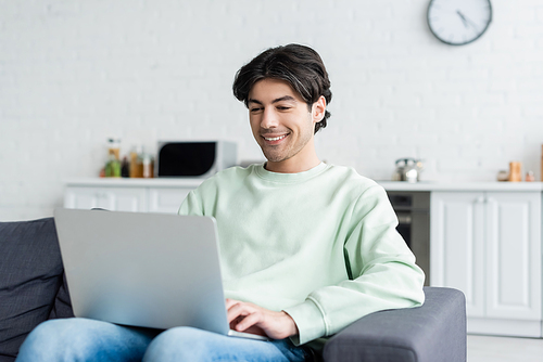 happy young man typing on laptop while sitting on couch at home